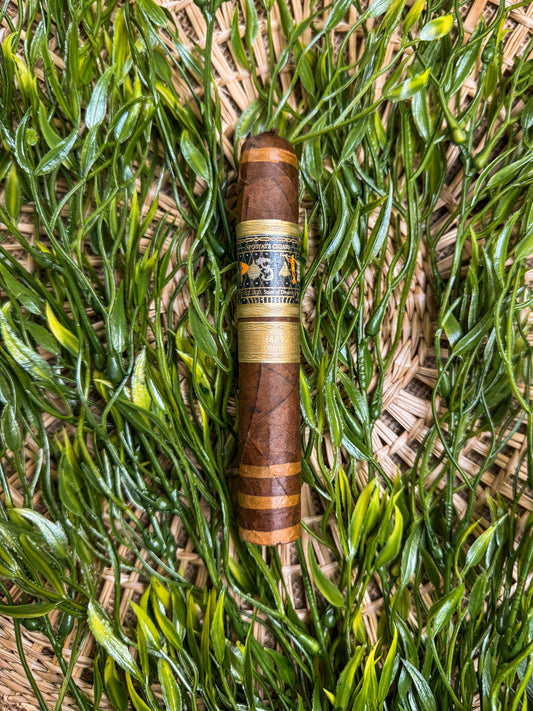 A single cigar resting on a bed of green tobacco leaves, with a band that reads 'The Deseret'.
