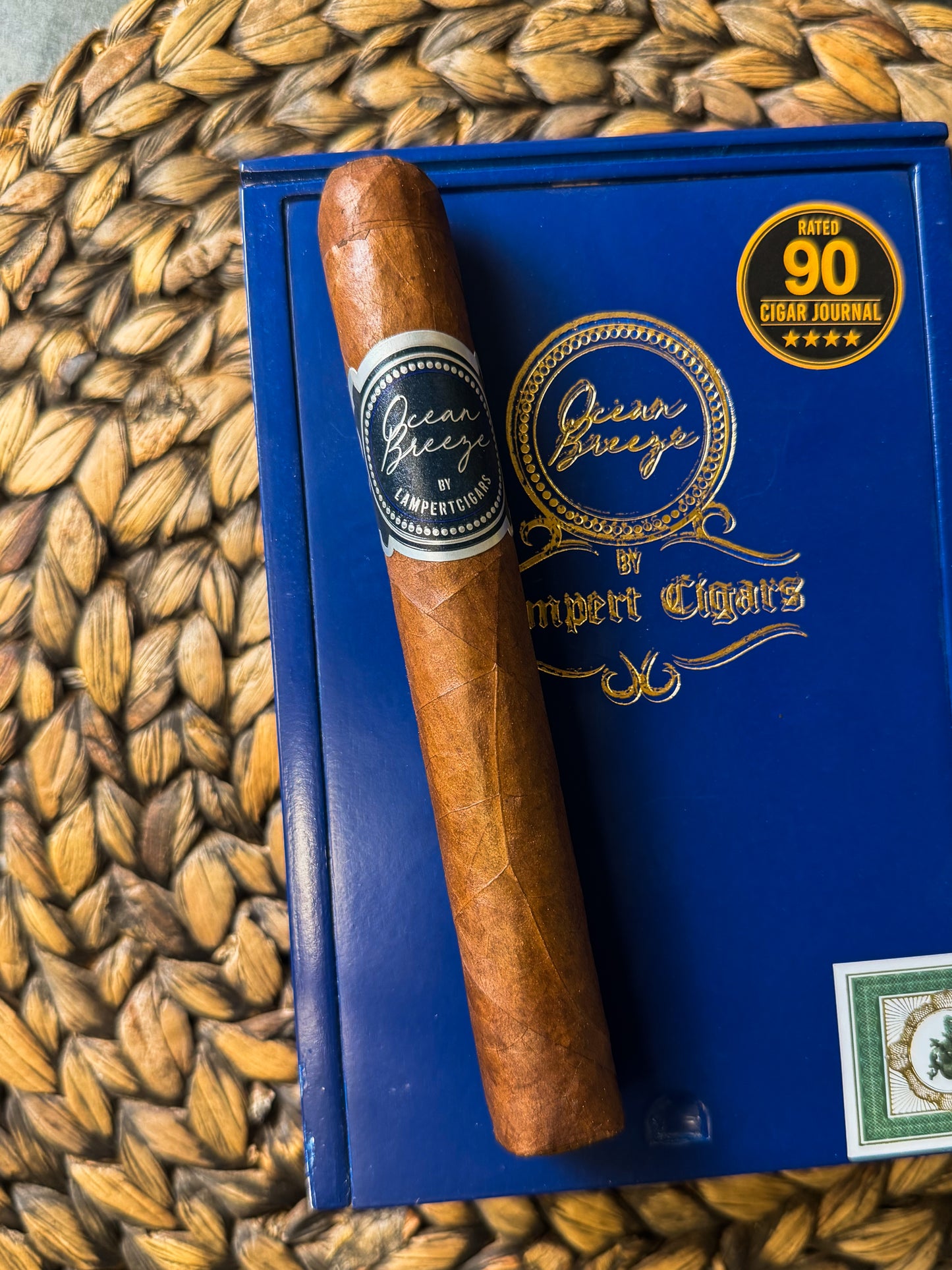 Cigar on a blue box with 'Queen Greco' branding on a woven mat background
