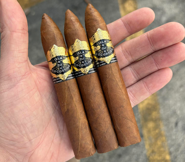 Three cigars with gold and black labels held in a hand against a blurred background