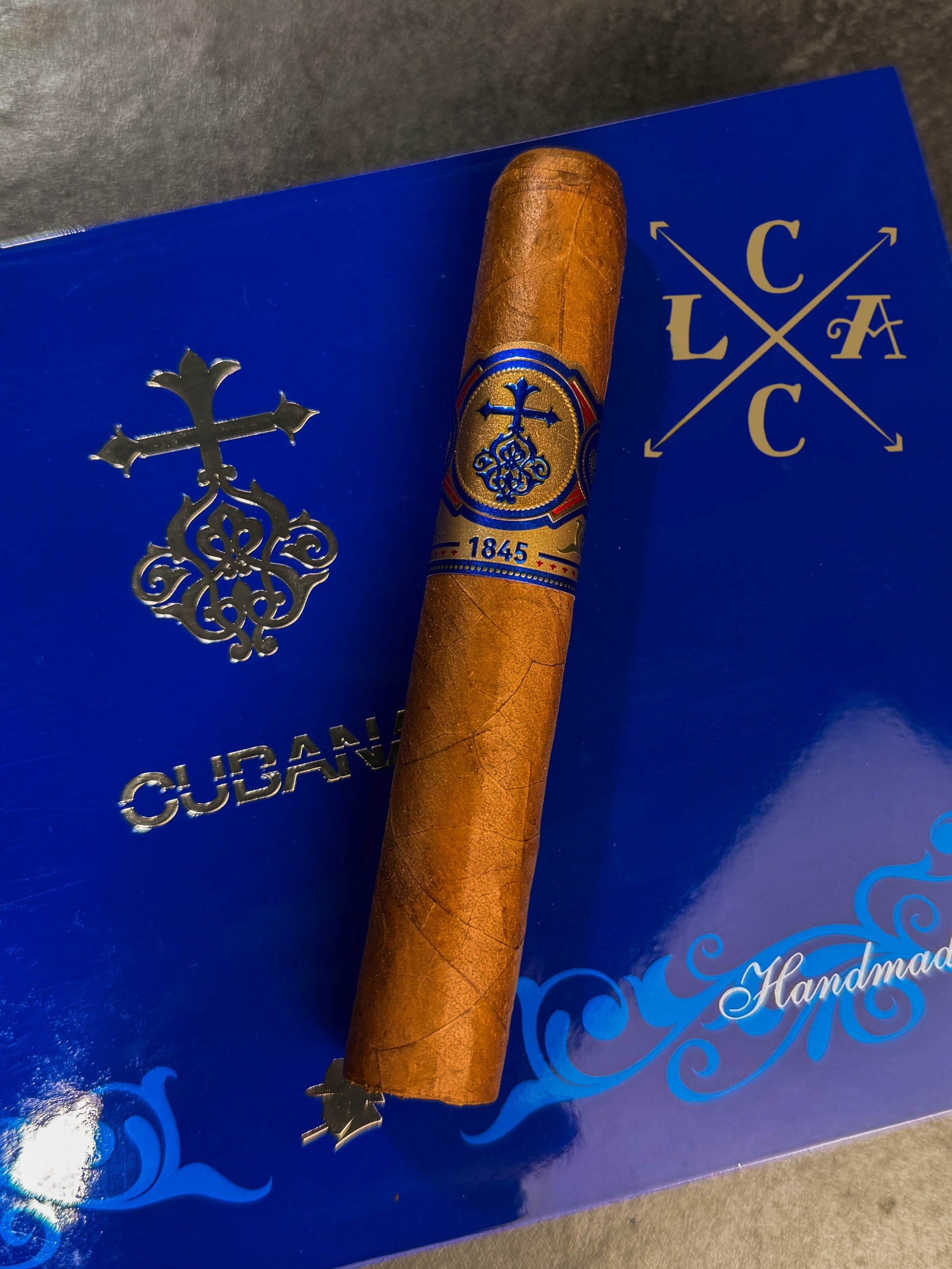 Cigar with blue band on a blue box labeled 'Cubana' and 'LCC'.