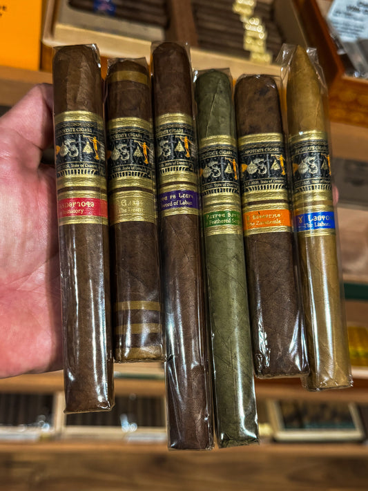 A collection of Apostate cigars displayed in a row with their bands visible, held by a person.