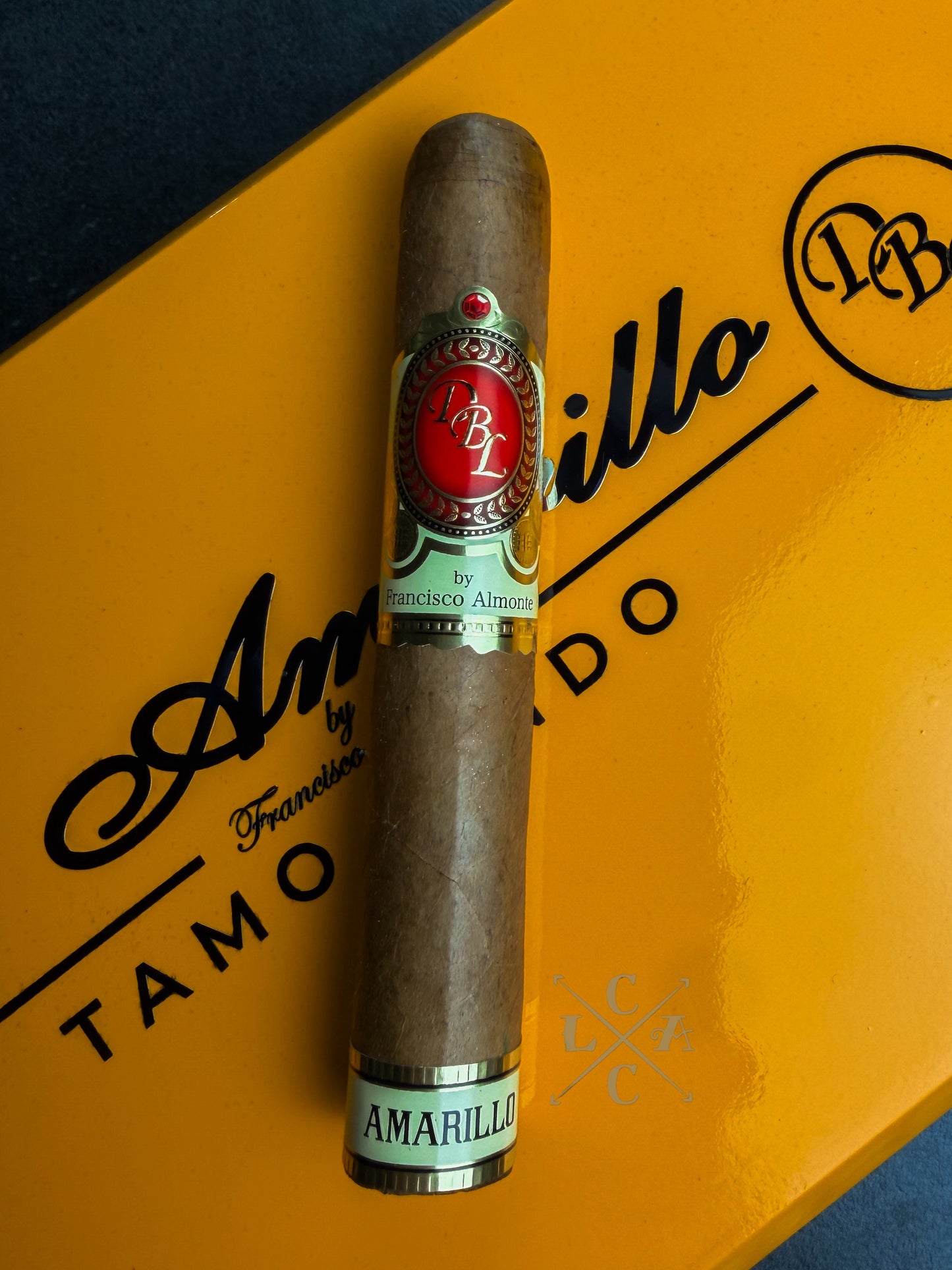 A single Amarillo cigar resting on its signature yellow and black packaging box, with the brand's logo clearly visible on both the band and the box.