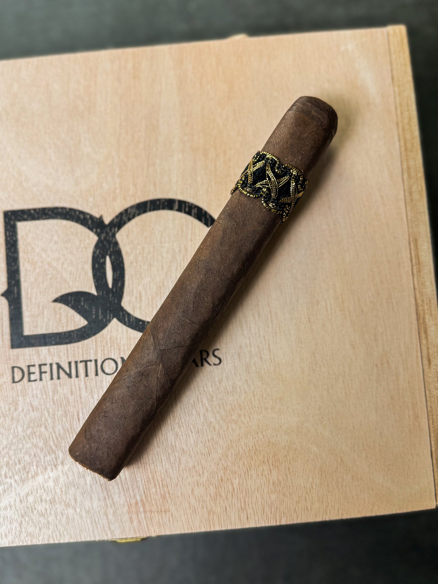 A single cigar resting on a wooden box with the text 'DEFINITION CIGARS'.