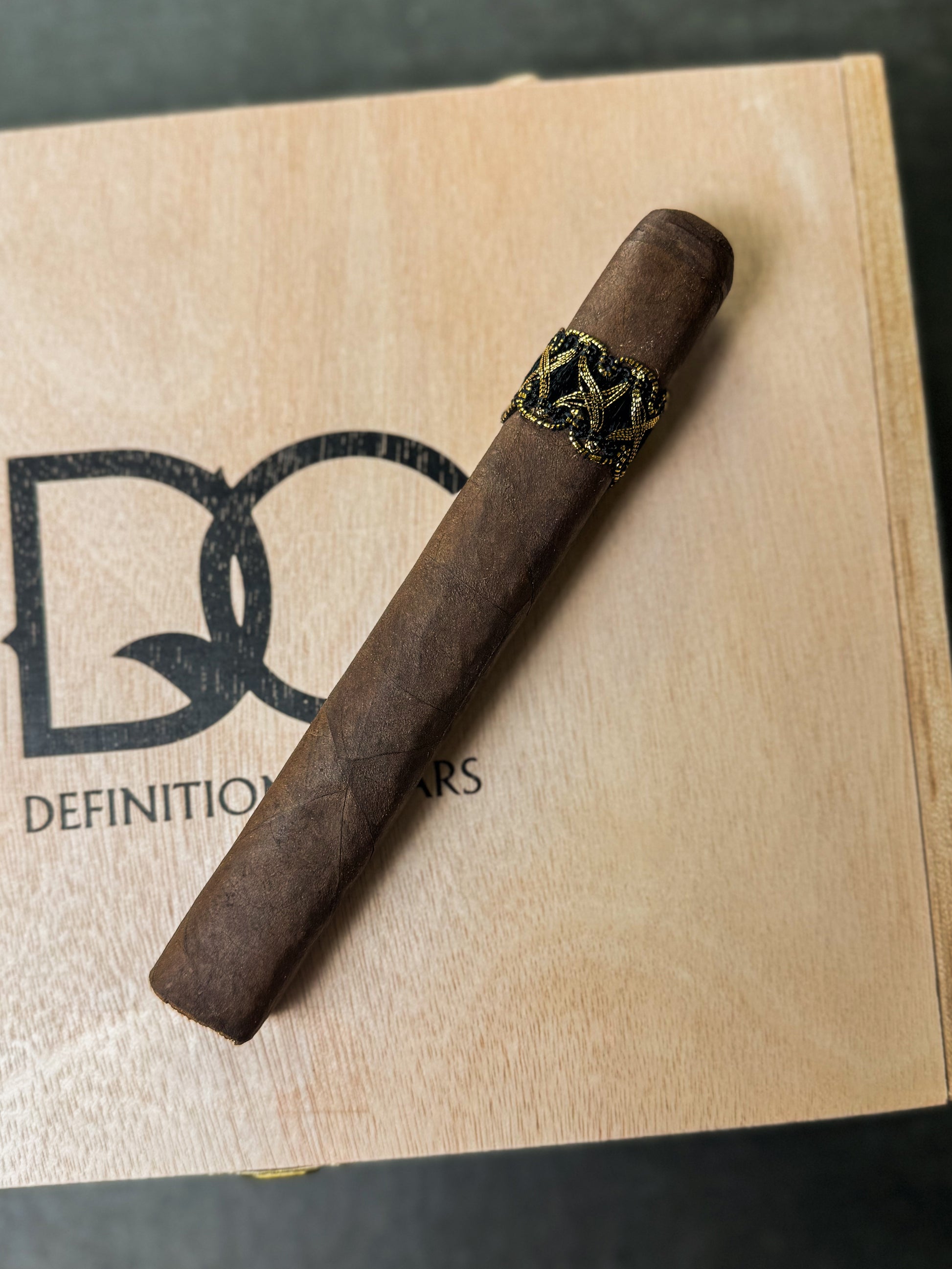 A single cigar resting on a wooden box with the text 'DEFINITION CIGARS'.