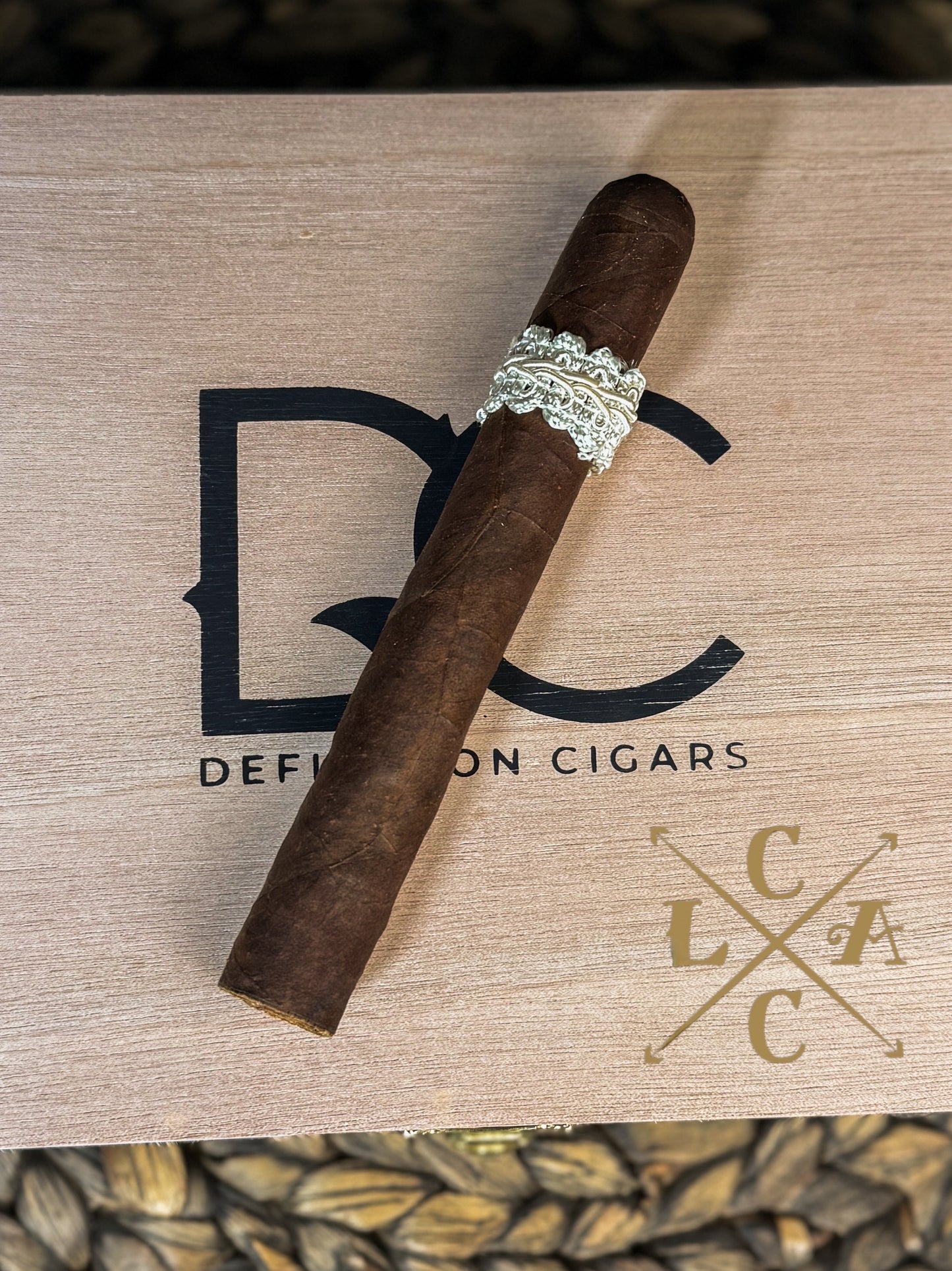 Cigar with a decorative band on a wooden surface with 'Defiance Cigars' branding.