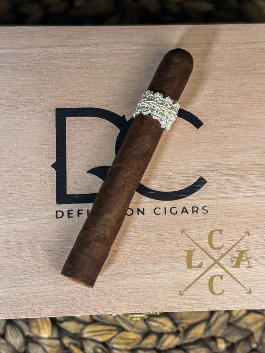 Cigar with a decorative band on a wooden surface with 'Defiance Cigars' branding.