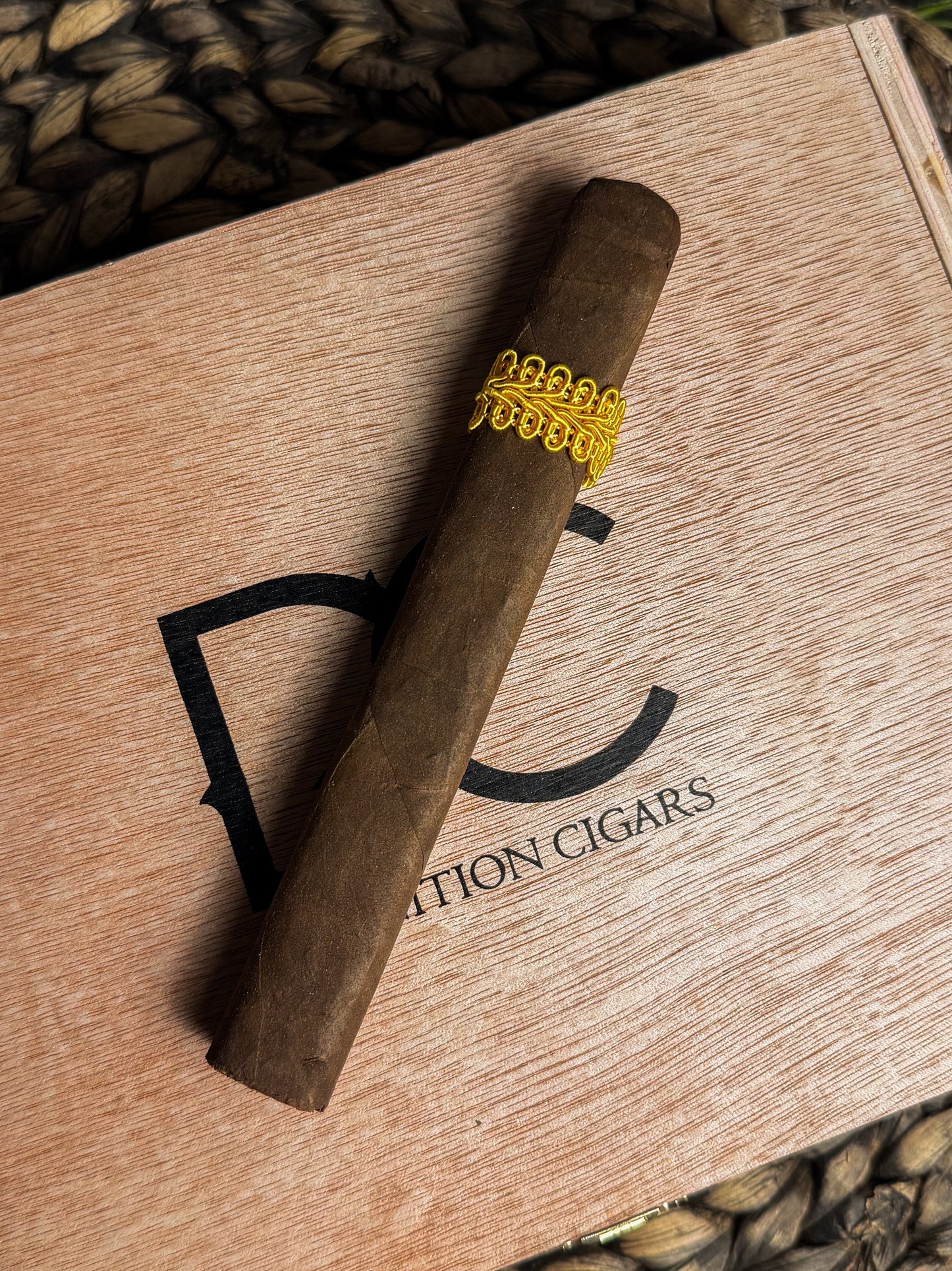 Cigar with a gold band on a wooden box labeled 'Definition Cigars'.