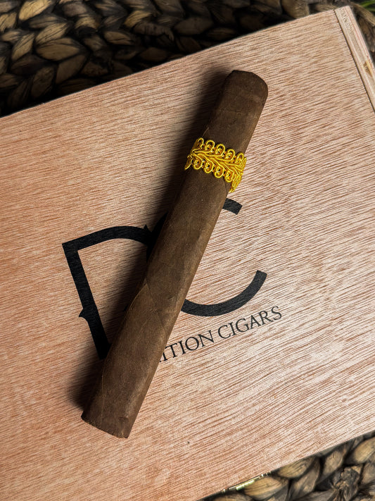Cigar with a gold band on a wooden box labeled 'Definition Cigars'.