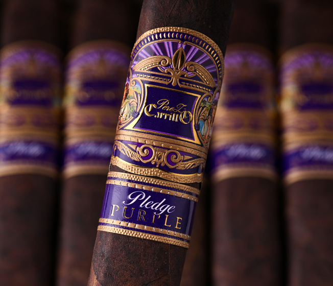 A close-up of a dark brown cigar with an ornate purple and gold band reading 'Prego PURPLE' and 'Royal Carriage,' with several matching cigars blurred in the background.
