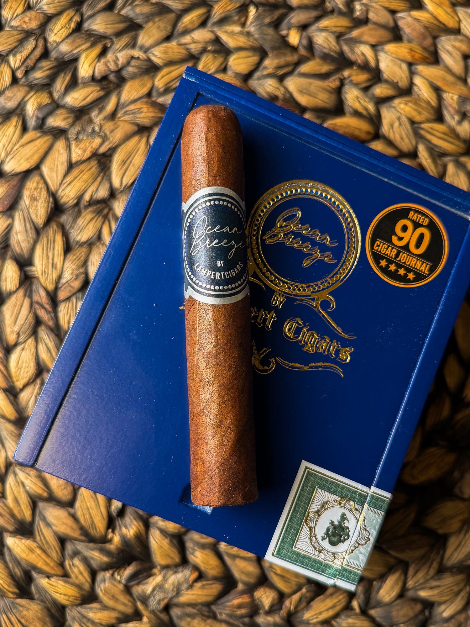 Cigar and blue box with brand logo on a woven surface