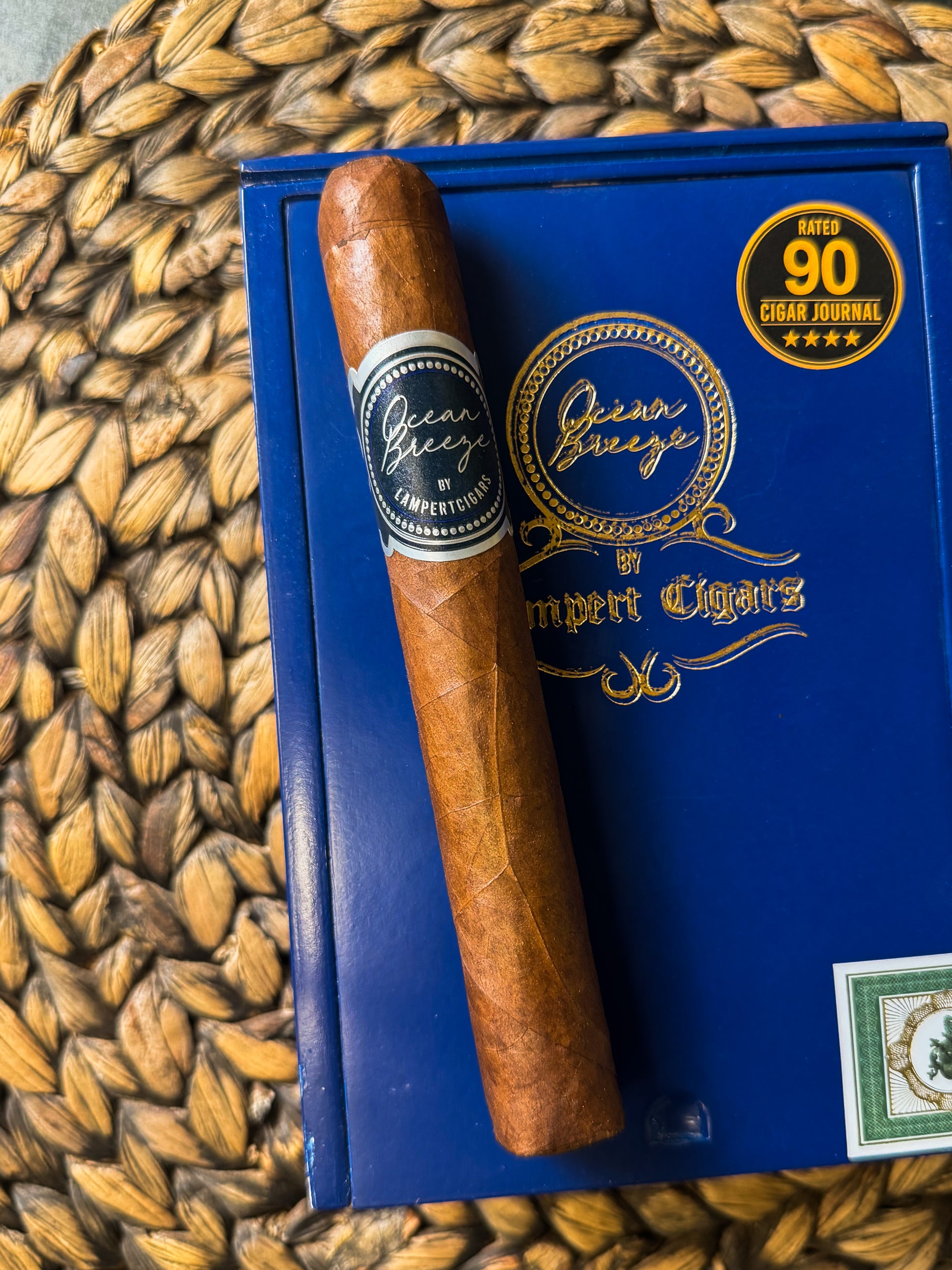 Cigar on a blue box with 'Queen Greco' branding on a woven mat background