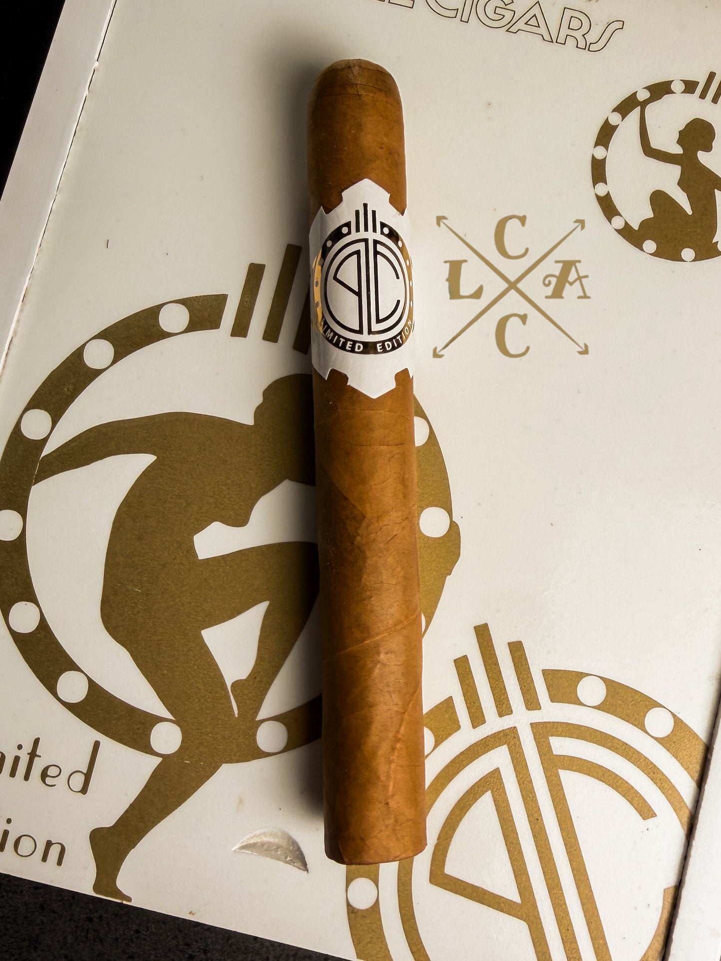 A single brown cigar with a white and black band reading 'Pabellon Clásico' rests on a white box decorated with gold graphics 