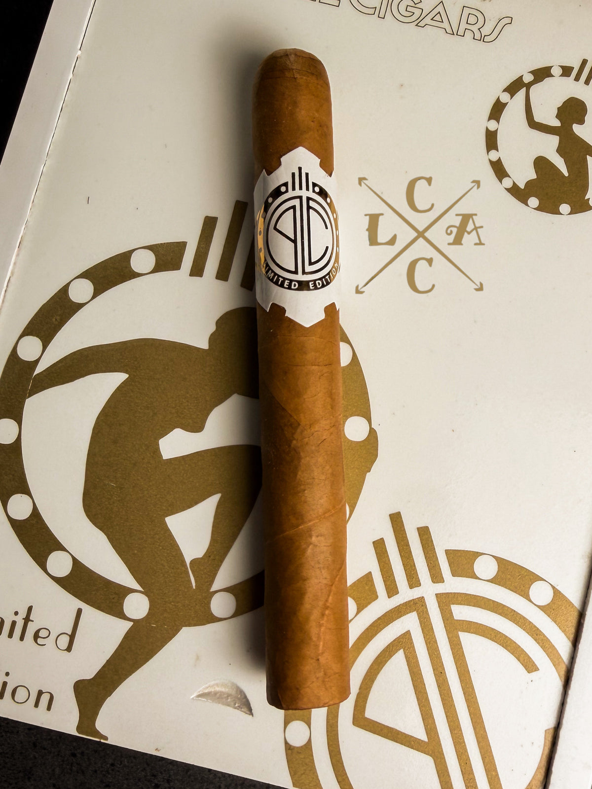 A single brown cigar with a white and black band reading 'Pabellon Clásico' rests on a white box decorated with gold graphics 