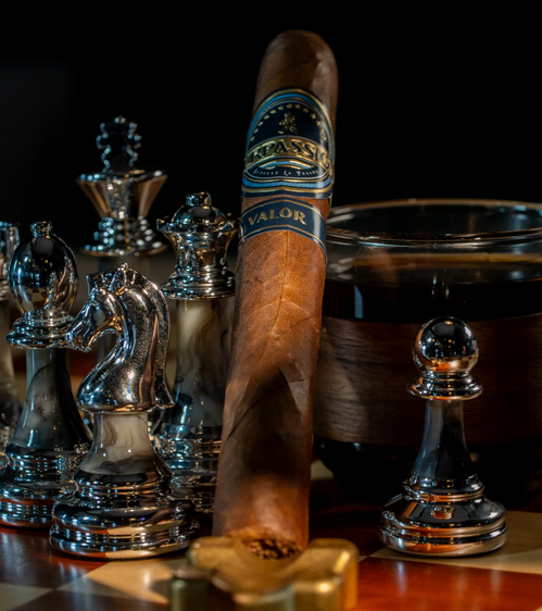 Cigar with a brand label on a chessboard with silver chess pieces and an ashtray.