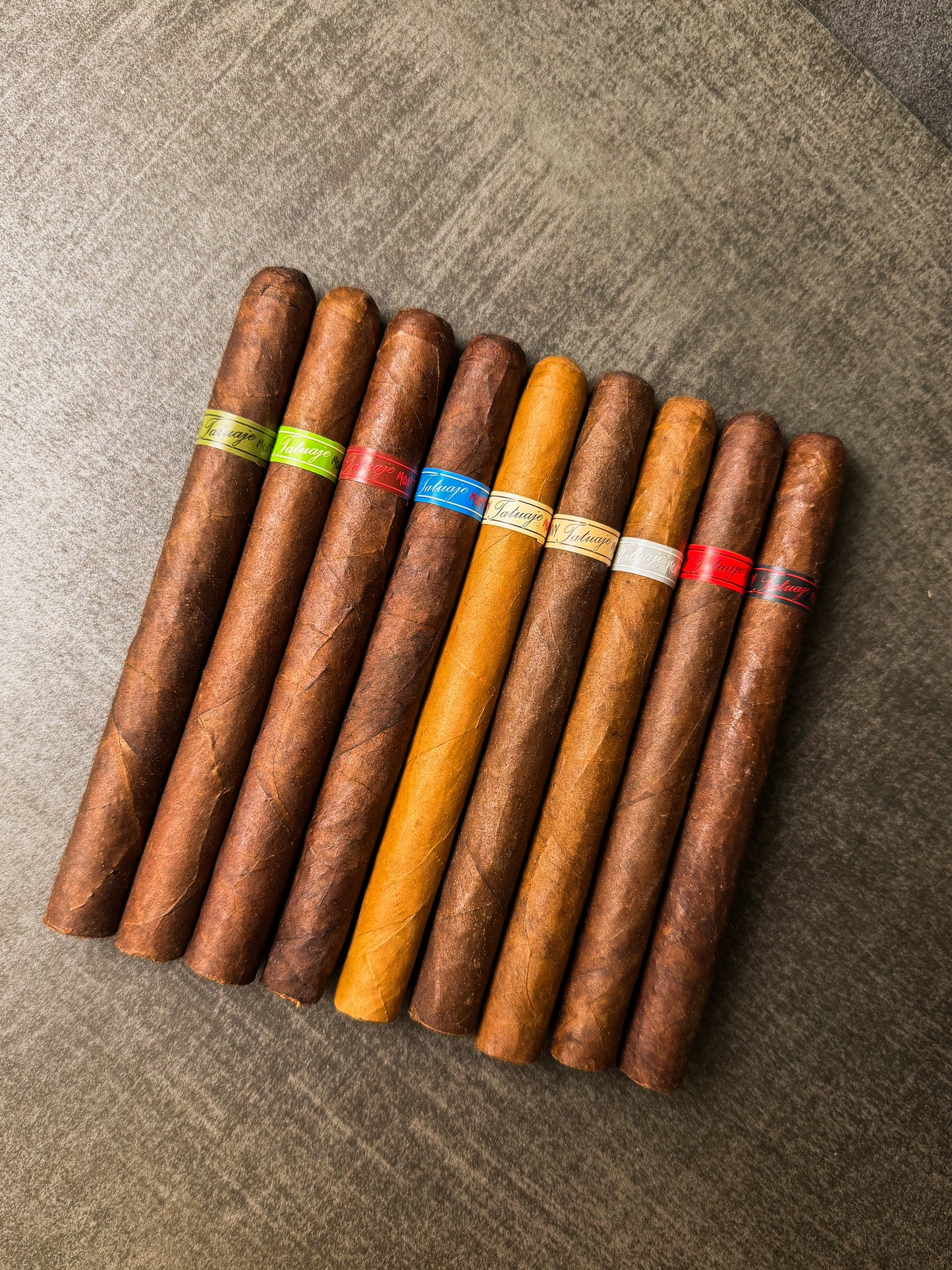 Assorted cigars with color-coded bands on a textured surface